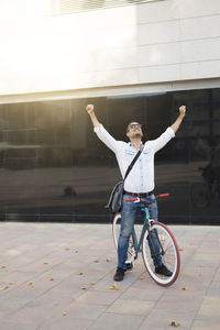 Mid adult man with bicycle standing against building