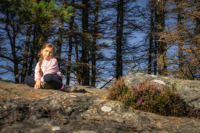 Girl sitting on a rock in a forest, illuminated by sunlight. glendalough, wicklow mountains, ireland