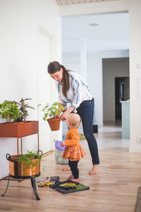 Fashion designer and daughter gardening while standing on hardwood floor at home