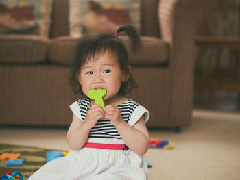Cute girl biting toy while sitting at home