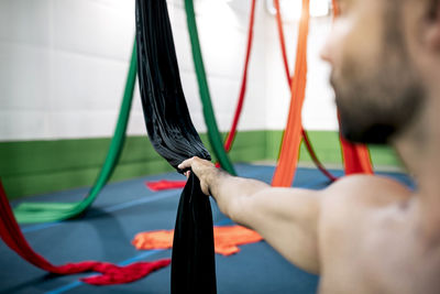 Crop muscular man grasping piece of black aerial silk during dance rehearsal in modern studio