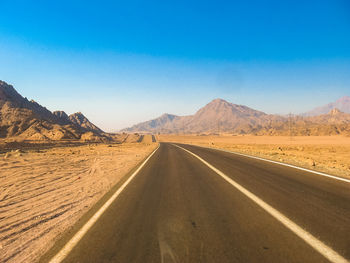 Empty road in desert against clear blue sky