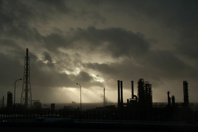 Silhouette factory against sky at sunset