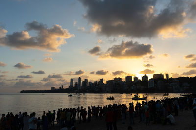 Group of people by sea against sky during sunset