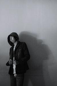 Man wearing hooded shirt while standing against wall