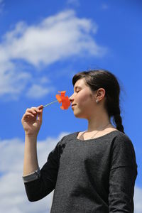 Close-up of young woman holding sunglasses against sky