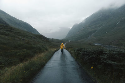 Rear view of woman running on country road in the scottish highlands