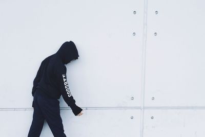 Side view of boy wearing hooded shirt standing against wall