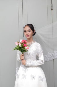 Portrait of bride holding bouquet against wall