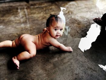 High angle view of naked of baby boy looking away while lying on wet floor