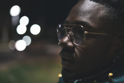 Close-up of man wearing eyeglasses in illuminated city at night