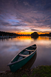 Boat moored on lake against sky during sunset