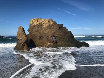 Mid distance view of woman standing by rock formations on shore