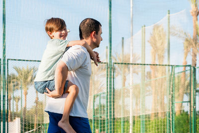 Happy father carrying son on back at sports ground