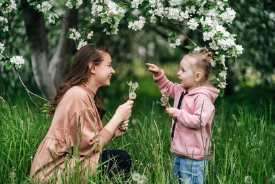 Mother and daughter with dandelions blooming apple trees