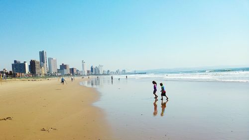 People walking at beach against clear sky