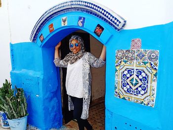 Portrait of woman wearing sunglasses while standing below blue arch