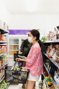 Asian woman with protective face mask with shopping basket in department store.