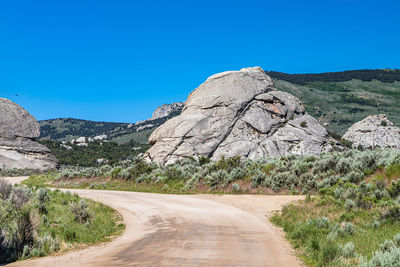 Road amidst rocky mountains against clear blue sky