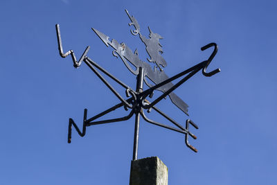 Low angle view of weather vane against clear blue sky