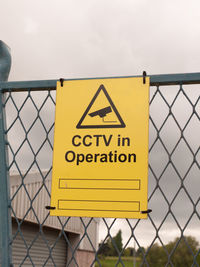 Close-up of yellow sign on metal against sky