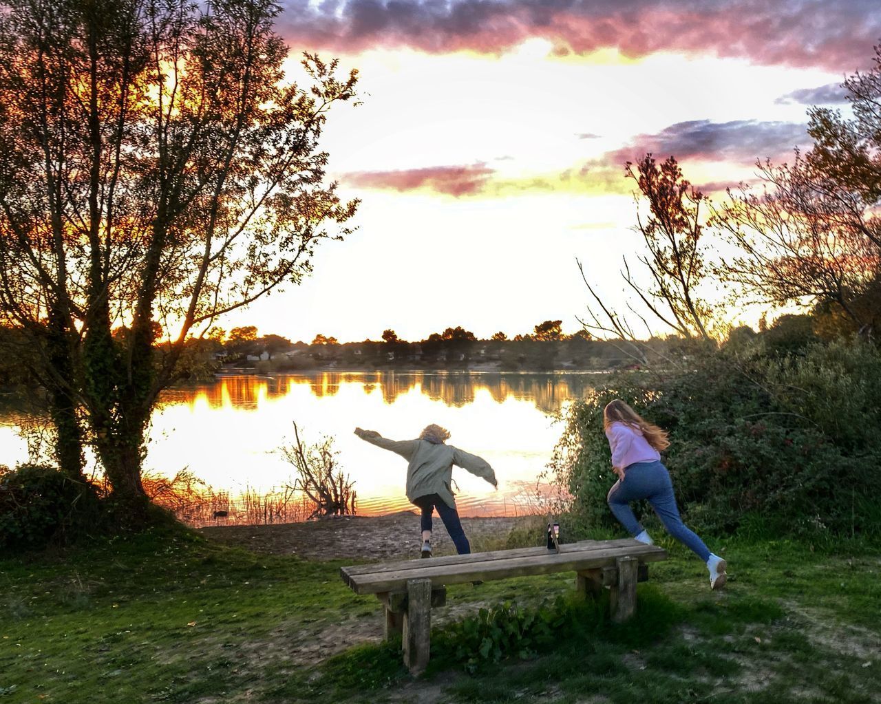 PEOPLE SITTING BY LAKE AGAINST SKY AT SUNSET