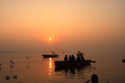 Silhouette people in sea against sky during sunset