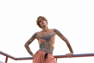 Low angle view of shirtless man standing on railing