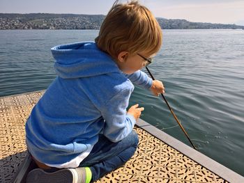 Boy holding stick by lake