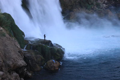Scenic view of waterfall with man standing on rock