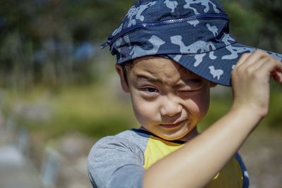 Close-up portrait of boy winking while wearing cap outdoors