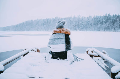 Person sitting on pier over frozen lake against trees