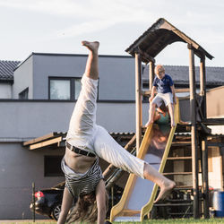 Teenage girl practicing cartwheel against brother on slide at playground