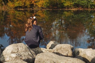 Rear view of girl sitting on rock by lake