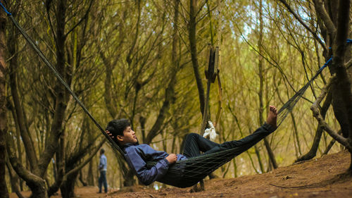 Side view of man sitting on tree trunk in forest