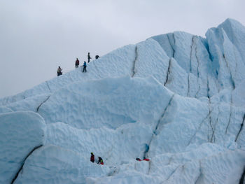 Unrecognizable ice climbers on glacial seracs silhouetted against a gray sky on matanuska glacier