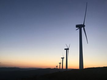 Silhouette wind turbines on field against sky during sunset