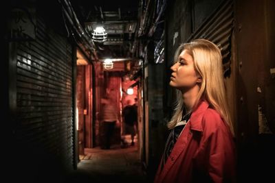 Young woman standing on street amidst shops in city at night