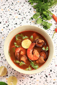 Top view tom yum gung with prawn, squid, and mushroom. served with corriander and lime