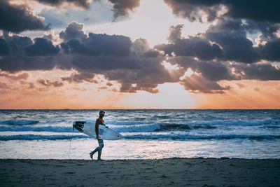 Full length of man on beach against sky during sunset