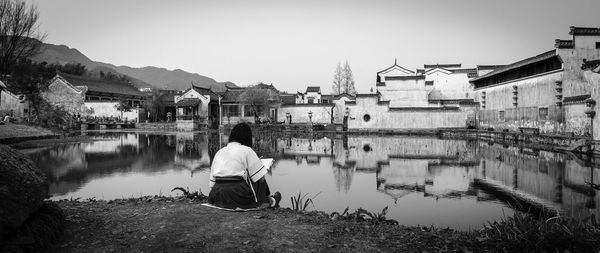 Rear view of girl sitting on lakeshore at village