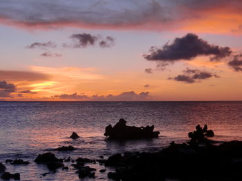 Silhouette rocks on sea against sky during sunset