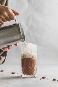 Cropped image of hand pouring milk in glass iced coffee cup on table