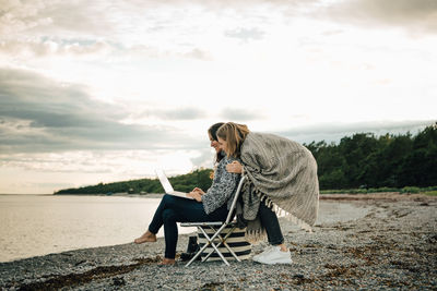 Woman sitting on chair at bench against sky