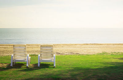 Empty chairs on beach against sky