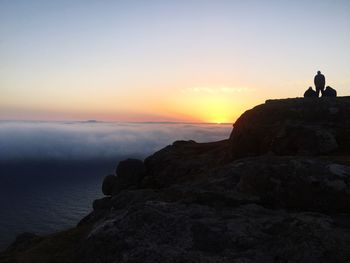 Silhouette of men standing on mountain against sky during sunset 