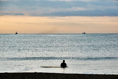 Silhouette man on surfboard in sea against sky during sunrise