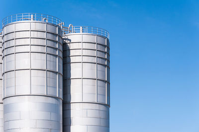 Low angle view of silos against clear blue sky