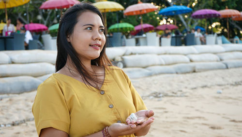 Smiling young woman holding seashell standing at beach