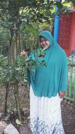 Portrait of woman standing by plants against trees